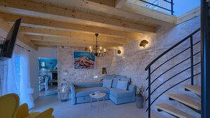 A modern living room with a blue sofa, a yellow armchair, a wooden staircase, and a stone wall. - House Bjankura (Smokvica)