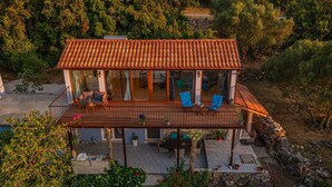 A two-story house with a tiled roof, a covered patio with seating, and a stone foundation. - House Bjankura (Smokvica)