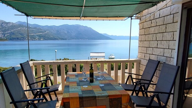 Eine Terrasse mit Tisch und Stühlen, mit Blick auf ein Gewässer und Berge.