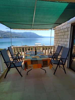 A terrace with a table and chairs, overlooking a body of water and mountains. - Apartment Ante (Korčula)