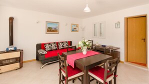 Um espaço de estar compacto com mesa de jantar, cadeiras, um sofá com manta vermelha, um pequeno aquecedor e uma porta de madeira.
