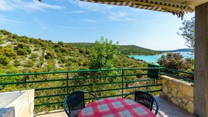 A balcony with a checkered table and chairs, overlooking a scenic landscape with hills and a body of water. - House Small Robinson (Marina)