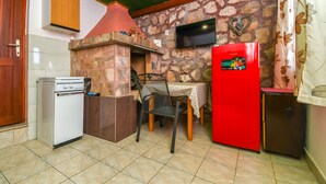 A kitchen with a stone wall, a TV mounted above a fireplace, a red refrigerator, and a dining table with chairs. - House Small Robinson (Marina)