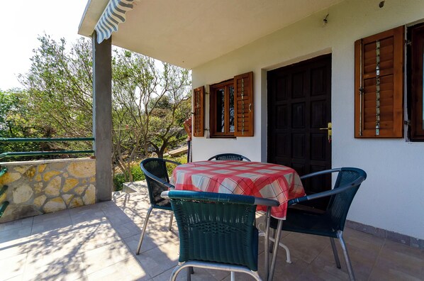 Une terrasse couverte avec une table et des chaises, un mur en pierre et une porte avec des volets en bois.