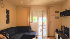A living room with a dark-colored sofa, a television on a stand, and a sliding glass door leading to an outdoor area. - Apartment Petra (Rab)
