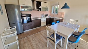 A modern kitchen with a stainless steel refrigerator, oven, and microwave. There is a dining table with blue chairs and a white tablecloth. - Apartment Petra (Rab)