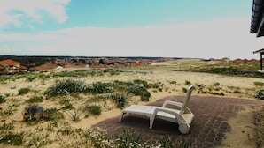 Vista de la playa con una silla de descanso blanca en un área pavimentada, con vistas a un pueblo costero de tejados rojos.