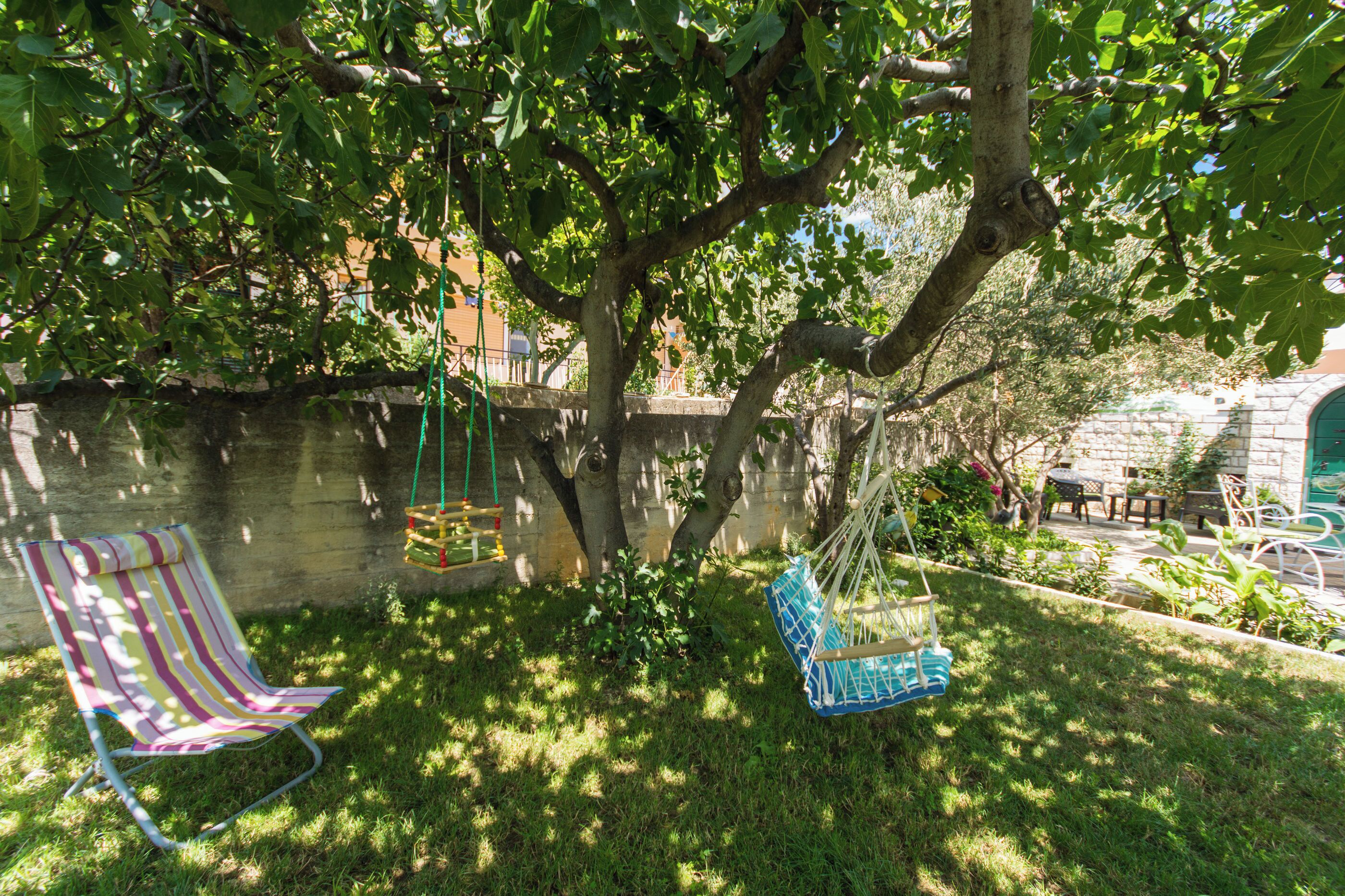 Un jardín con un columpio, una silla a rayas y un macetero colgante.