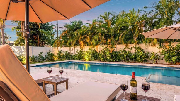 Un espace aménagé au bord de la piscine, avec des chaises longues et une table sur laquelle se trouvent des verres à vin et une bouteille.