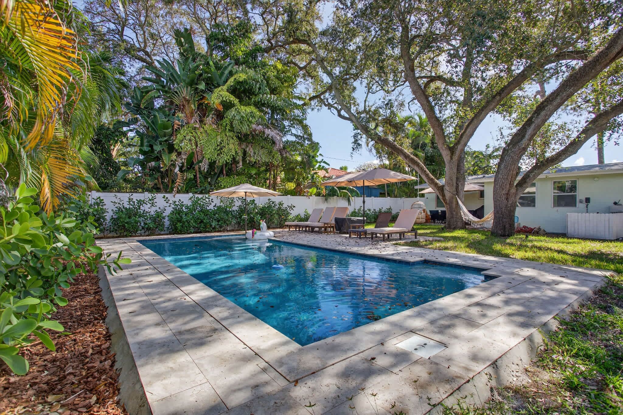 Piscina retangular com deck revestido, rodeada por vegetação exuberante e árvores.