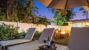 Un espace patio aménagé avec deux fauteuils, une petite table sur laquelle se trouvent une bouteille de vin et deux verres, ainsi qu’un foyer extérieur.