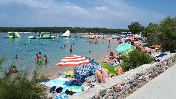 Una spiaggia con persone che nuotano e prendono il sole, giochi gonfiabili e ombrelloni.
