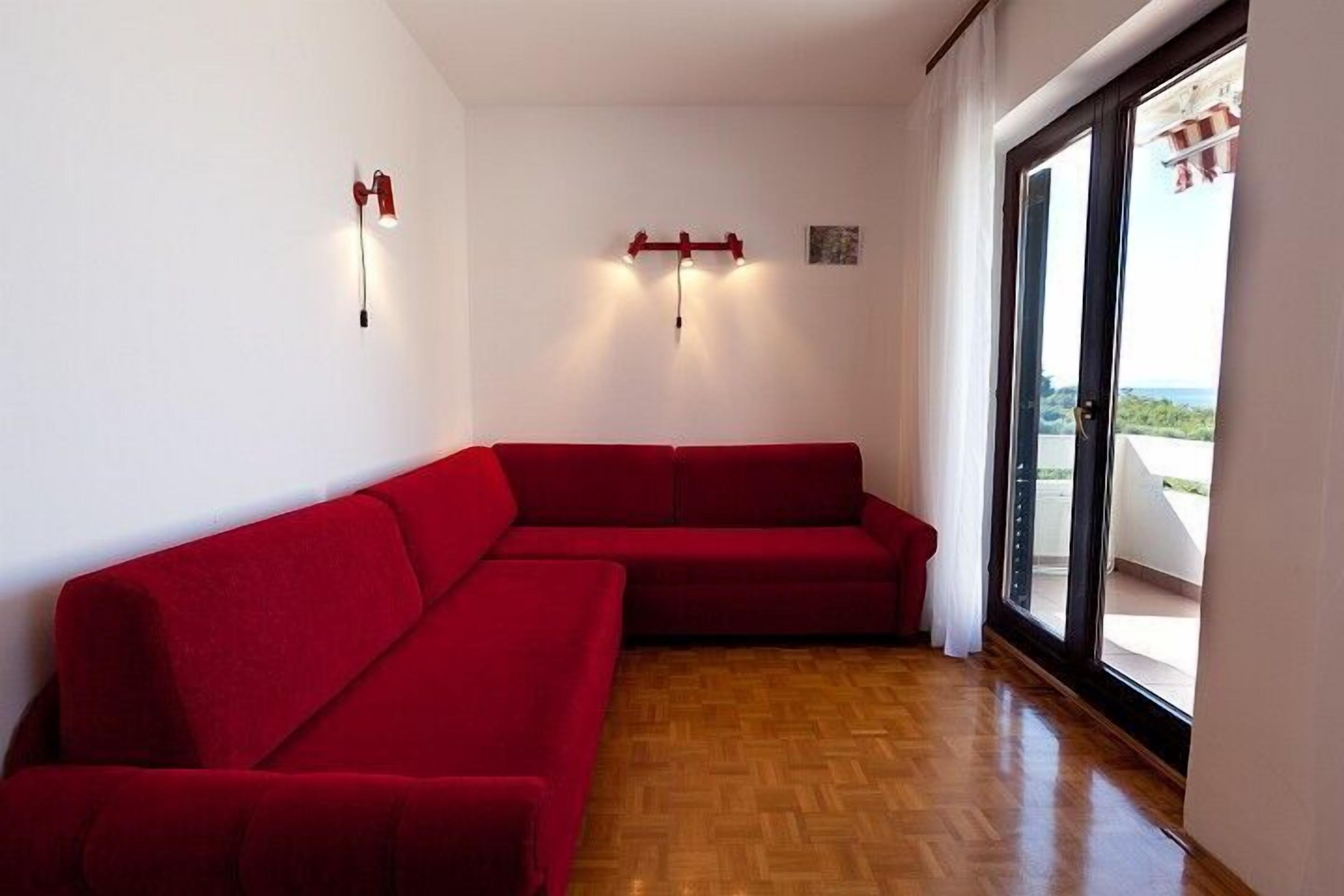 A room with a red sofa, a wooden floor, and a sliding glass door leading to an outdoor area.