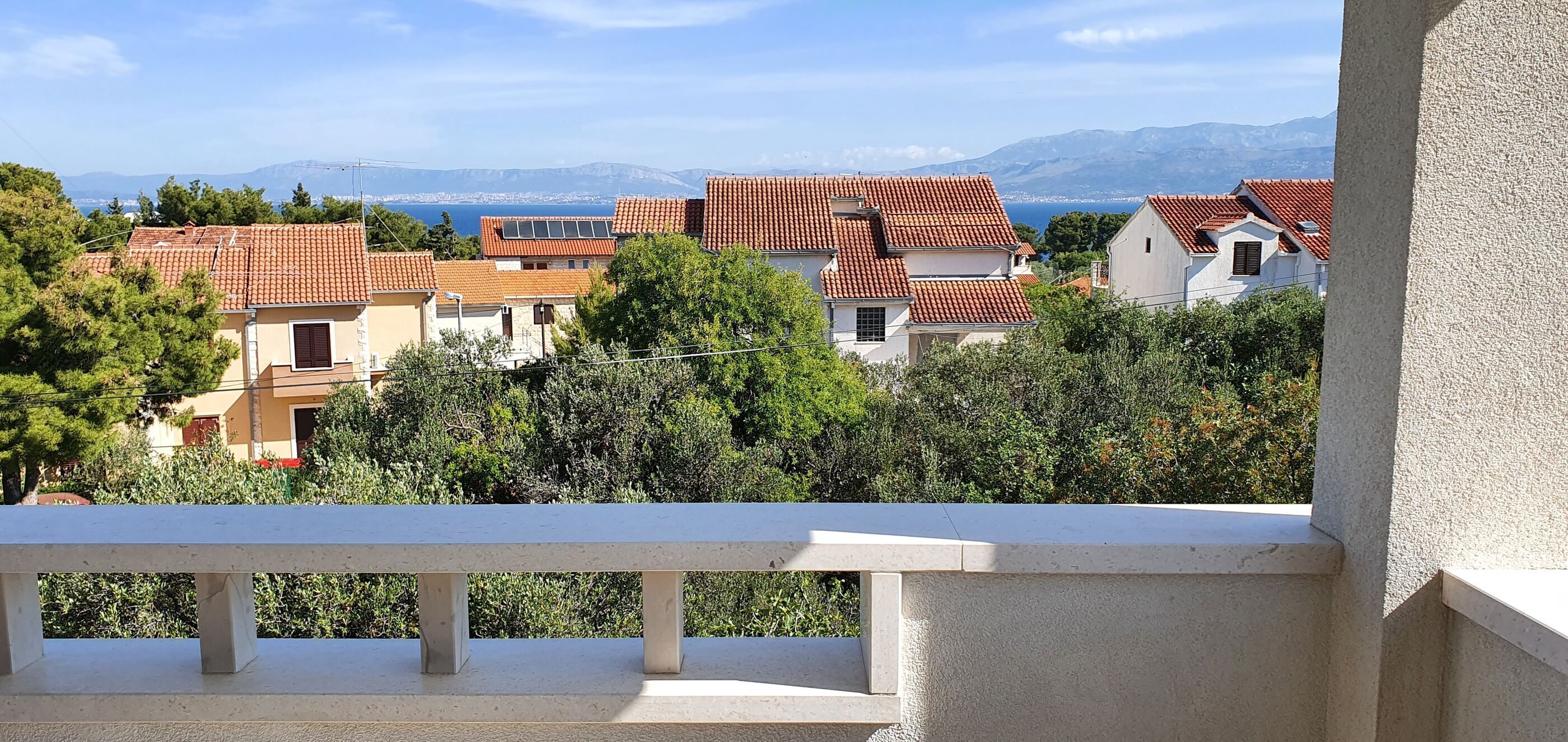 Un quartier résidentiel où les maisons se distinguent par leurs toits recouverts de tuiles rouges et offrent une vue sur la mer et les montagnes en arrière-plan.
