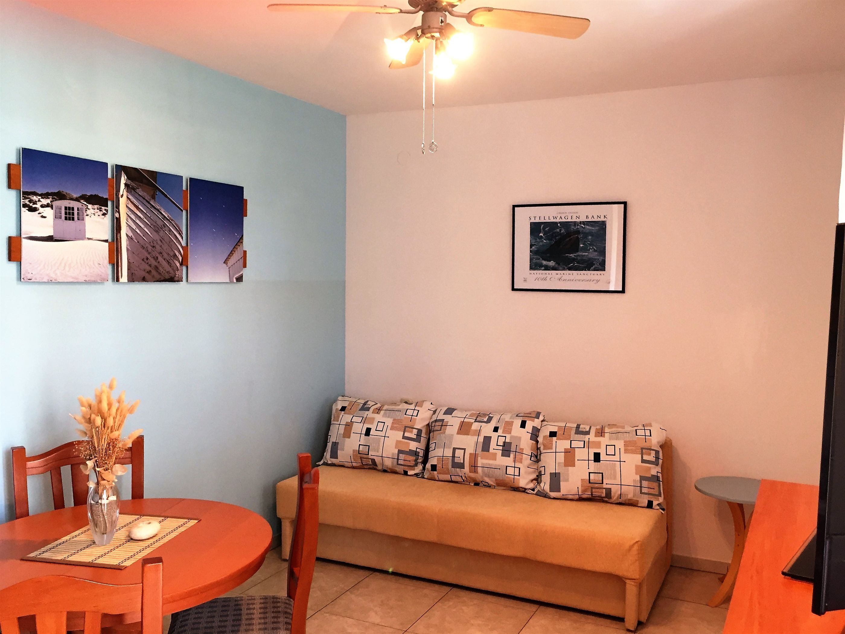 Une pièce comprenant un canapé, une table à manger avec des chaises, un ventilateur de plafond et des tableaux encadrés accrochés au mur.