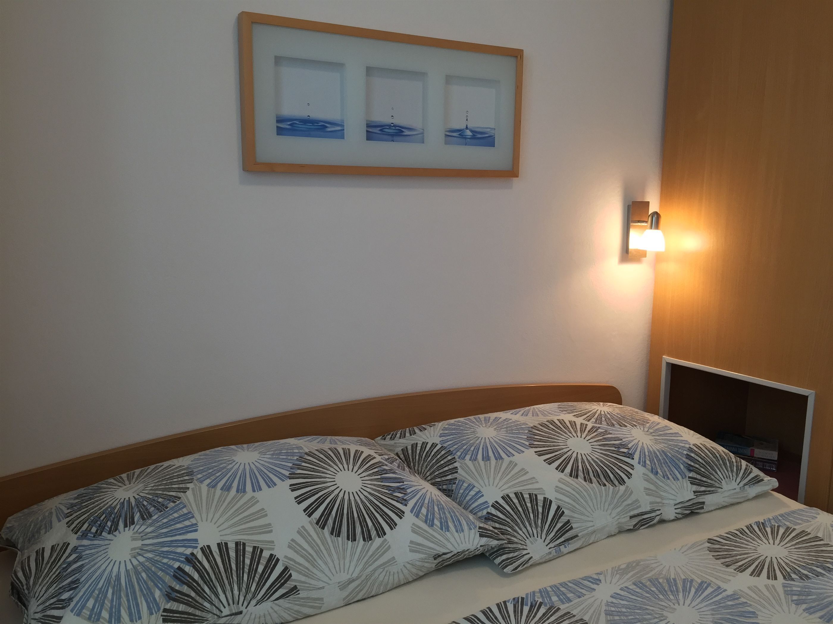 Een hotelkamer met een bed met een geborreld beddegoed, een aan de muur bevestigd fotolijstje en een bedlamp.