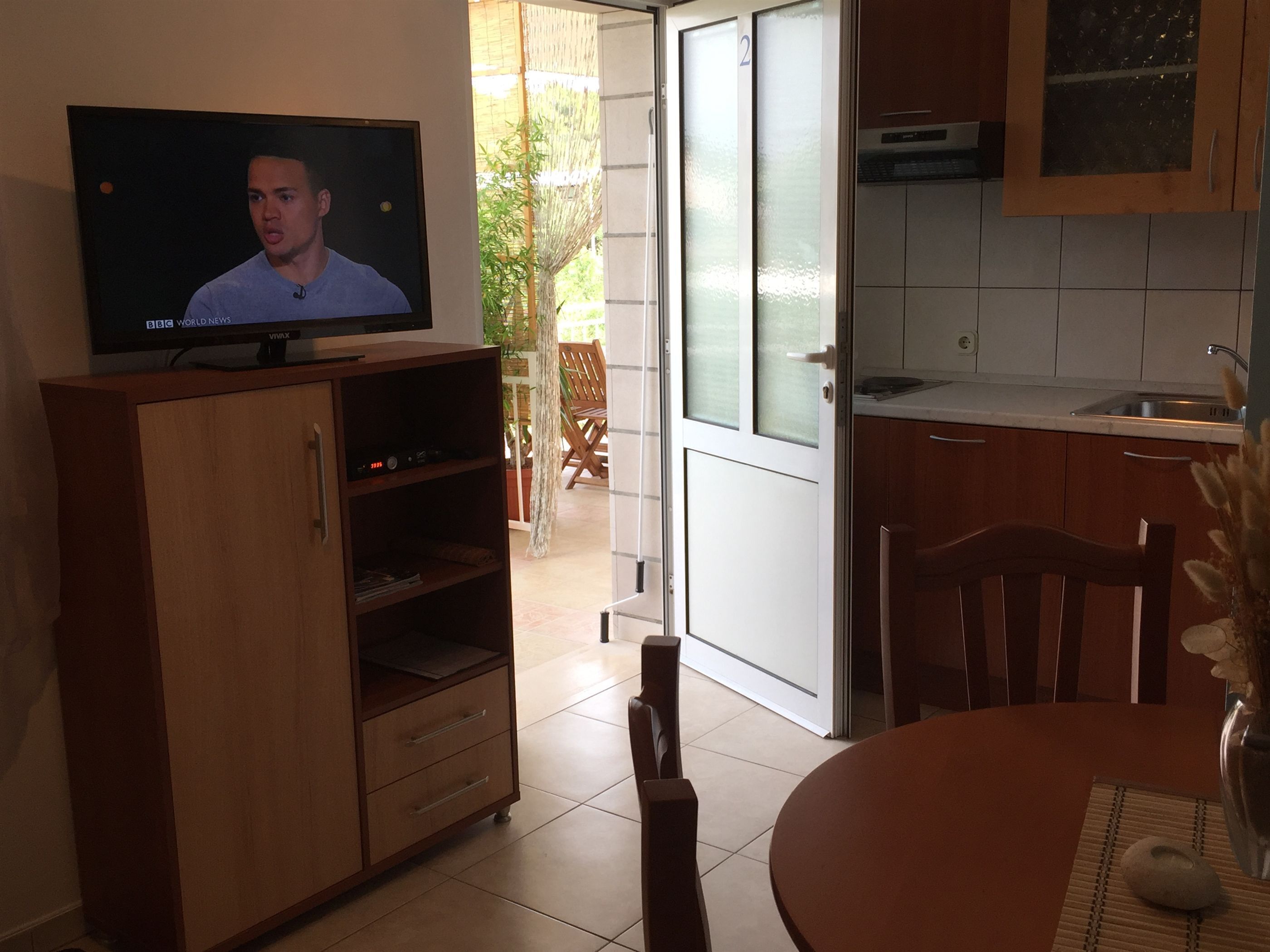 Una cocina con televisor sobre un mueble de madera, una mesa de comedor con sillas y una encimera de cocina.