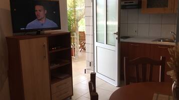 Una cocina con televisor sobre un mueble de madera, una mesa de comedor con sillas y una encimera de cocina.