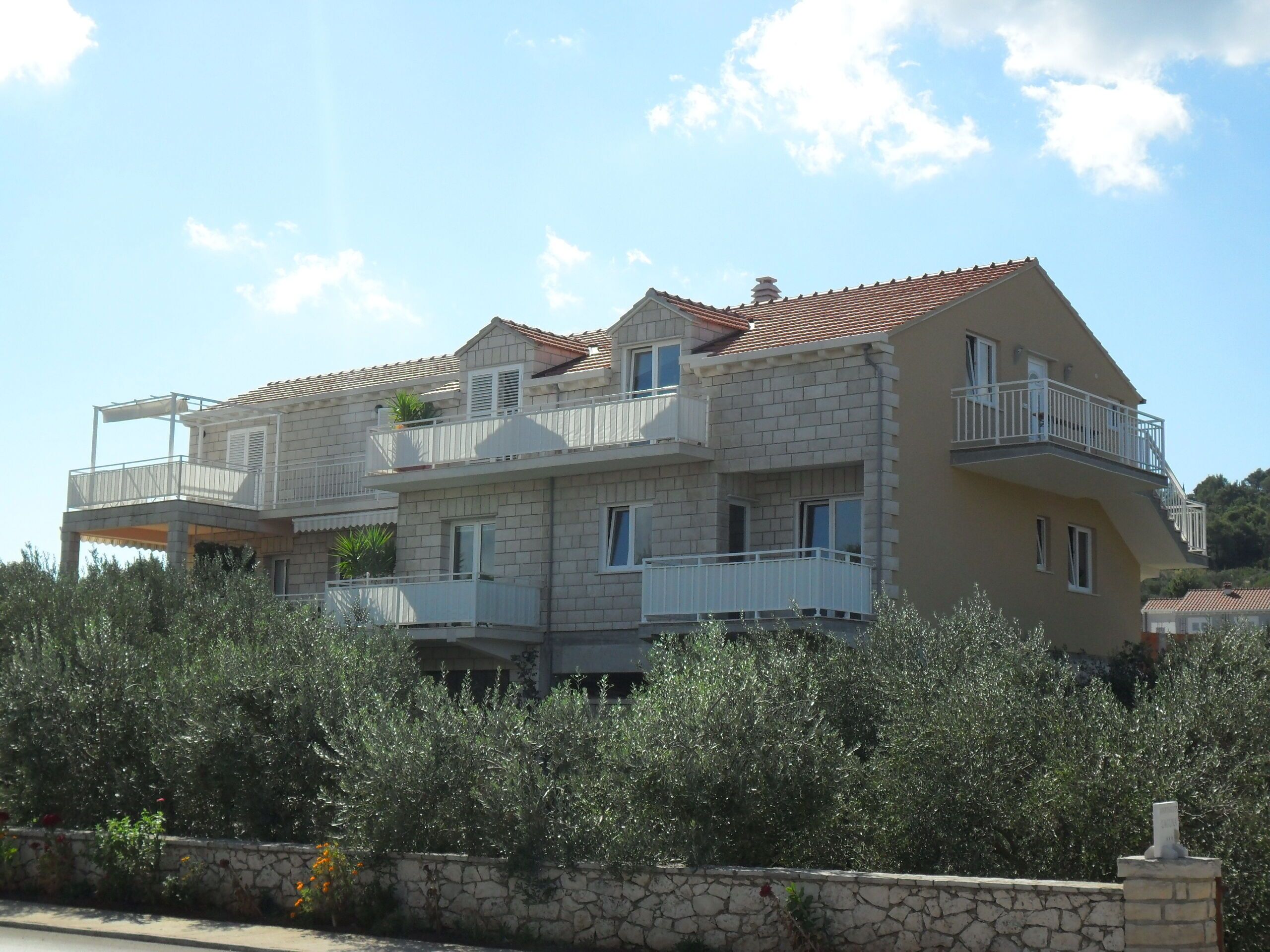 Un immeuble résidentiel à plusieurs étages, doté de balcons, avec un mur de pierre à l’avant et un ciel dégagé.