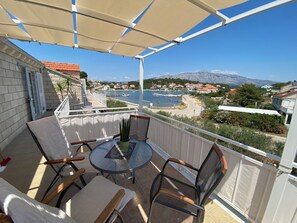 A balcony with a table and chairs, overlooking a coastal town with houses and a marina. - Apartments Zeljko (Lumbarda)
