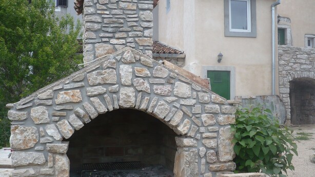 A stone-built outdoor oven with a chimney, surrounded by a stone wall and greenery. - House Dragica (Cres)