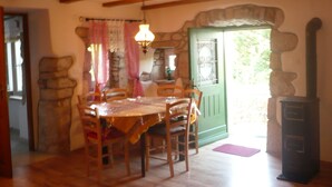 A dining area with a wooden table and chairs, a stone wall, a green door, and a fireplace. - House Dragica (Cres)