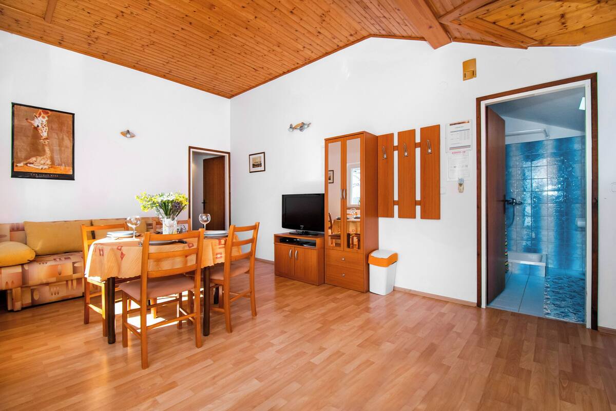 A living room with a wooden ceiling, a dining table with chairs, a sofa, a TV, and a cabinet.