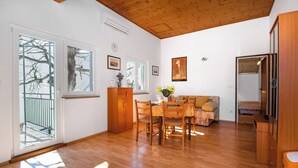 A spacious room with a wooden floor, a dining table with chairs, a sofa, and a wooden cabinet. - Apartments Family Corner (Vodice)