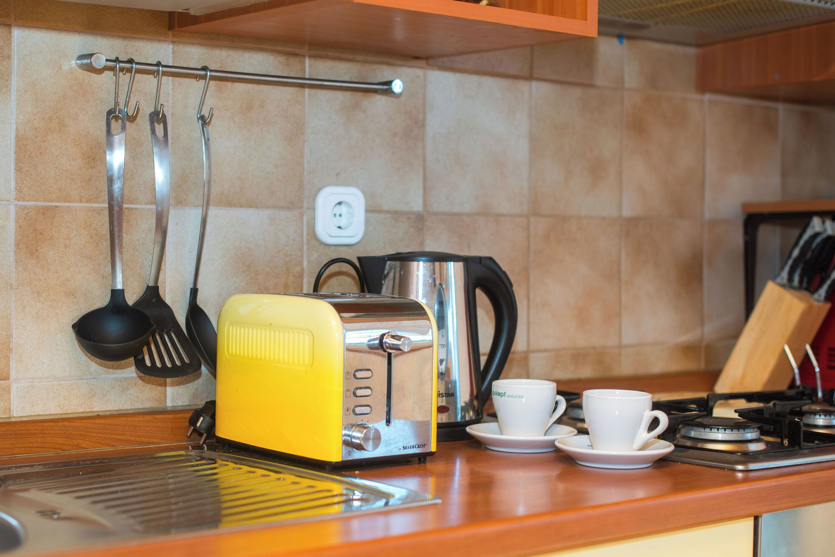 A kitchen with a yellow toaster, a coffee maker, and two white cups on the counter.