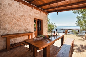 Ein Steinhaus mit Holztisch und -bänken, einer Holztür und Blick auf das Meer.