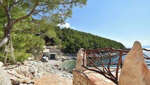 A stone pathway leading to a rustic building with a view of the sea and a forested hill. - House Robinzon Sea Beauty (Jelsa)