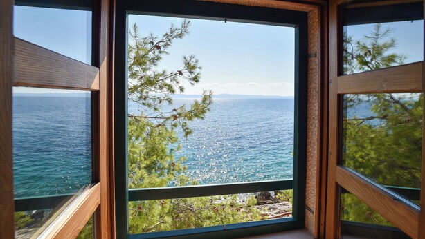 A view through a window with a wooden frame, overlooking a body of water and a distant shoreline. - House Robinzon Sea Beauty (Jelsa)