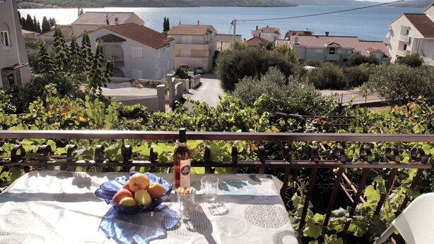 Un balcon avec une table dressée pour un repas, donnant sur un quartier résidentiel avec des maisons et un plan d’eau.