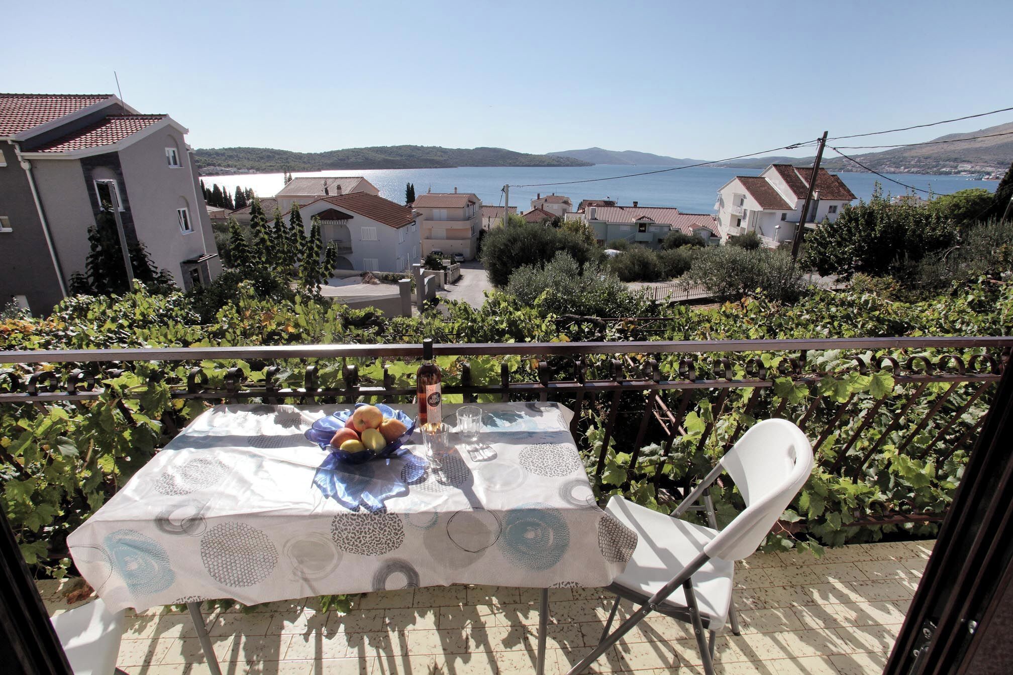 A balcony with a table set for two, overlooking a vineyard and a lake.