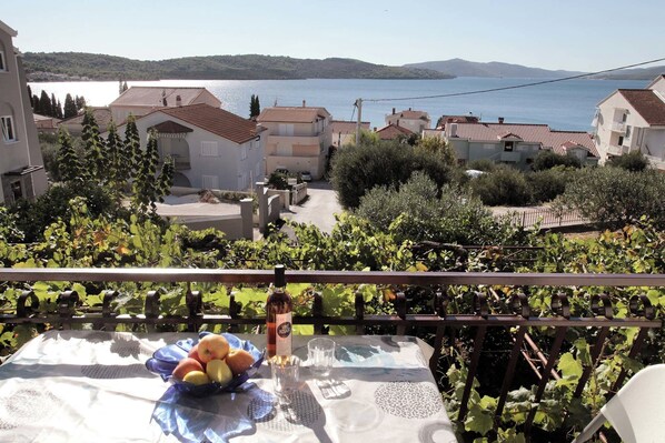 Ein Balkon mit Esstisch, der Blick auf ein Küstendorf mit Häusern und Weinbergen freigibt.