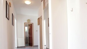 Un couloir avec un banc en bois, des murs blancs et une porte au fond.
