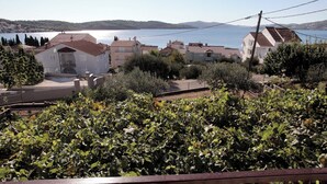 Un vignoble avec des rangées de vignes, des maisons aux toits de tuiles rouges et une étendue d’eau en arrière-plan.
