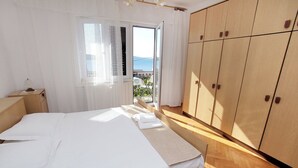 Une chambre à coucher avec un lit, une table de chevet, une armoire et une vue sur la mer par la fenêtre.
