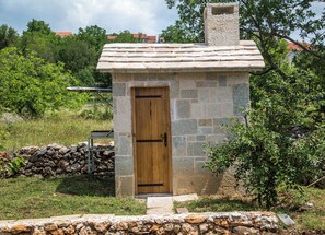 A stone-built structure with a wooden door, surrounded by a stone wall and vegetation. - House Bosnic (Cista Provo)