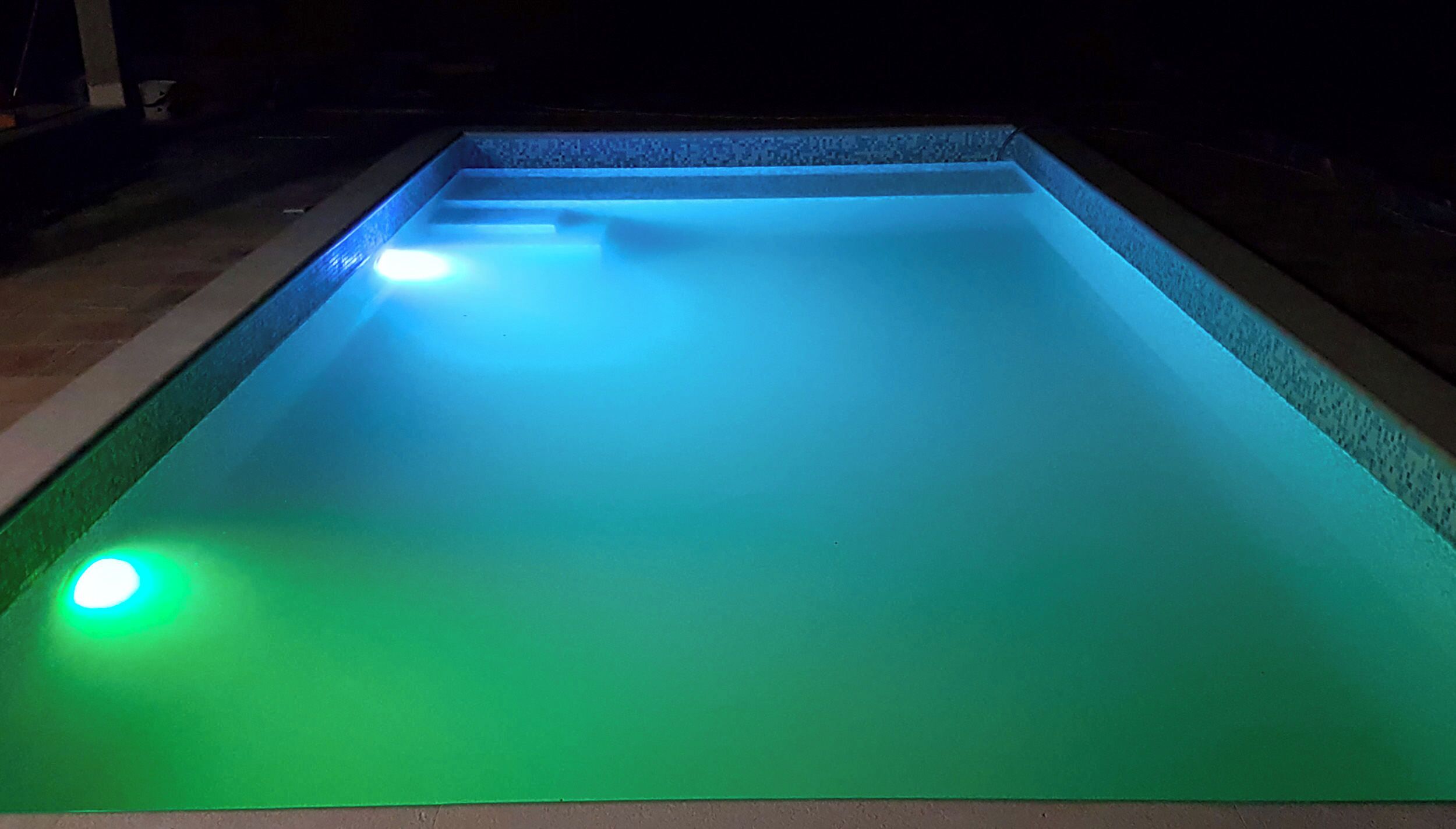 Une piscine rectangulaire à la surface lisse, illuminée par une lumière bleue qui se reflète sur l’eau.