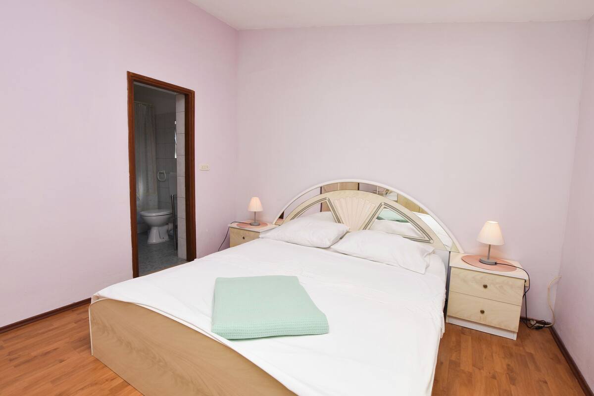Une chambre à coucher comprenant un lit, deux tables de chevet, une commode, un miroir et une porte donnant sur une salle de bain.