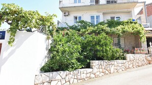 Un edificio de varios pisos con balcón, pared de piedra y vegetación.