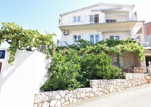 Un edificio de dos plantas con balcón, pared de piedra y vegetación.