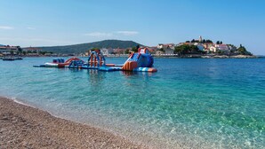 Una zona costera con agua cristalina, una playa de guijarros y coloridas estructuras inflables.