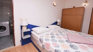 Un dormitorio con una cama, dos mesitas de noche, un armario, una lavadora y un aplique de pared.