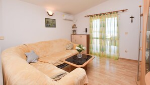 Una sala de estar con un sofá color beige, una mesa de centro con un jarrón, un mueble de madera y una ventana con cortinas de gasa.