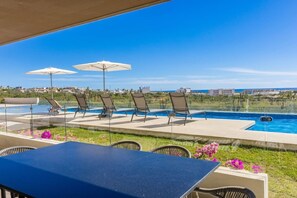 Ein Poolbereich mit Liegestühlen und Sonnenschirmen, mit Blick auf einen klaren blauen Himmel und eine entfernte Skyline.