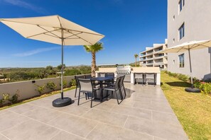 Eine Terrassengruppe mit Tisch, Stühlen, einem Grill und Sonnenschirmen.