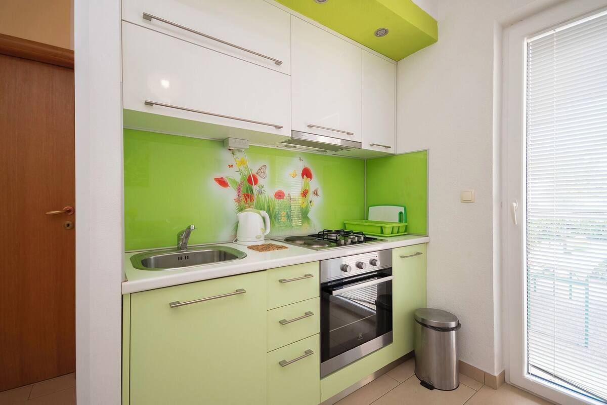 Une cuisine compacte avec un crédence vert, des armoires blanches, un évier en acier inoxydable, une cuisinière à gaz et un four.