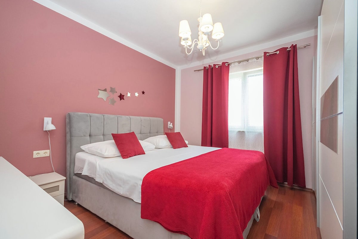 Une chambre à coucher avec un lit, une table de chevet, un lustre et une fenêtre avec des rideaux.